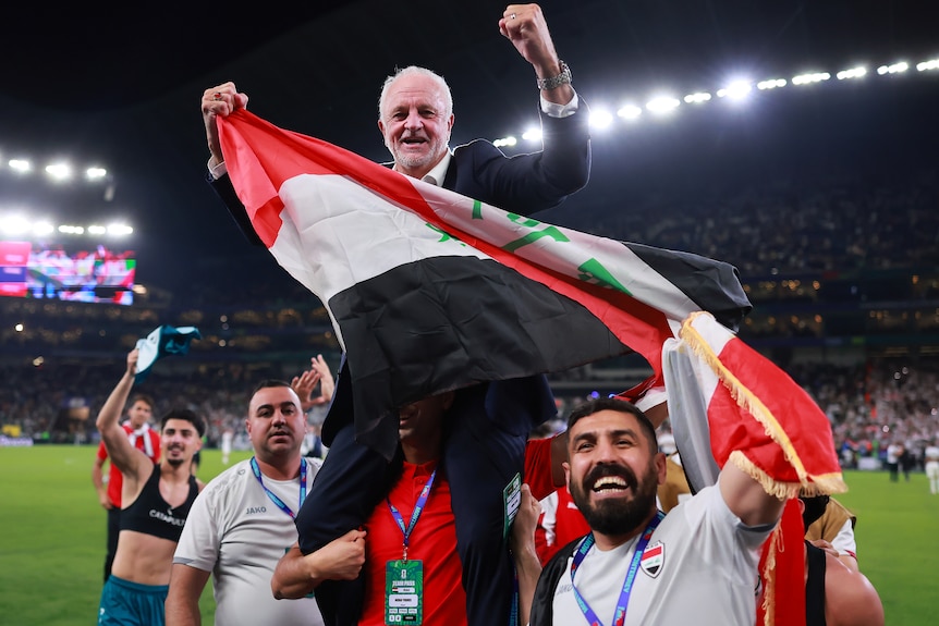 Iraq men's football coach Graham Arnold is sitting on the shoulders of his coaching staff, waving the Iraq flag
