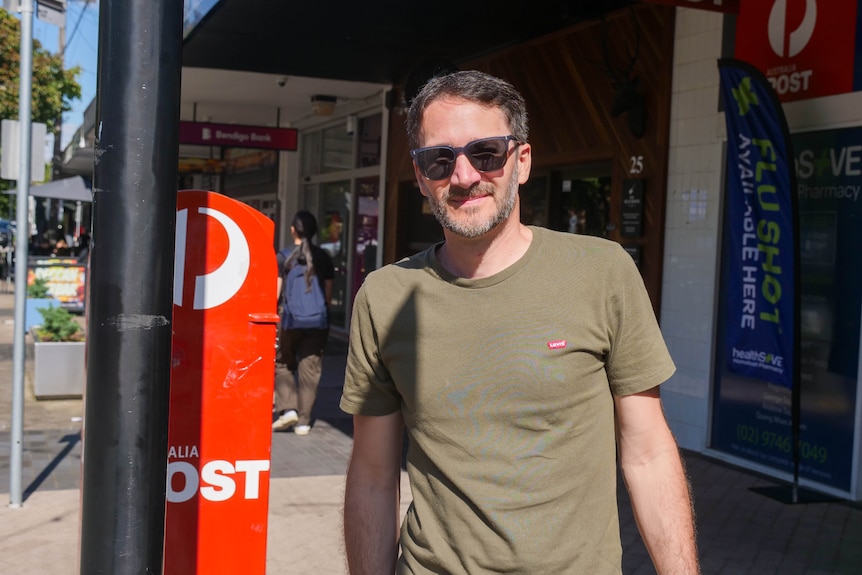 a man in a green t-shirt smiles gently on a suburban shopping street