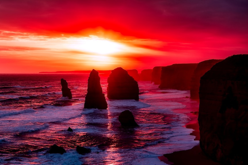 Large limestone monoliths and coastal cliffs silhouetted in red afternoon glow.
