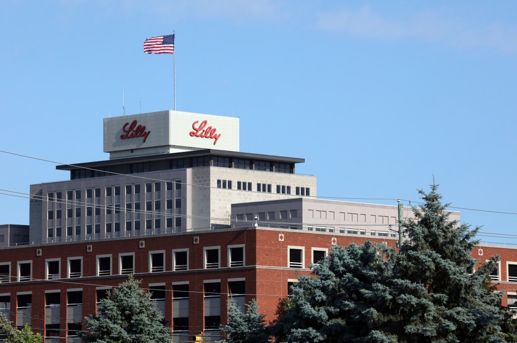 Exterior of the Eli Lilly and Company headquarters building in Indianapolis, Indiana, with the Lilly logo on the rooftop and an American flag flying above.