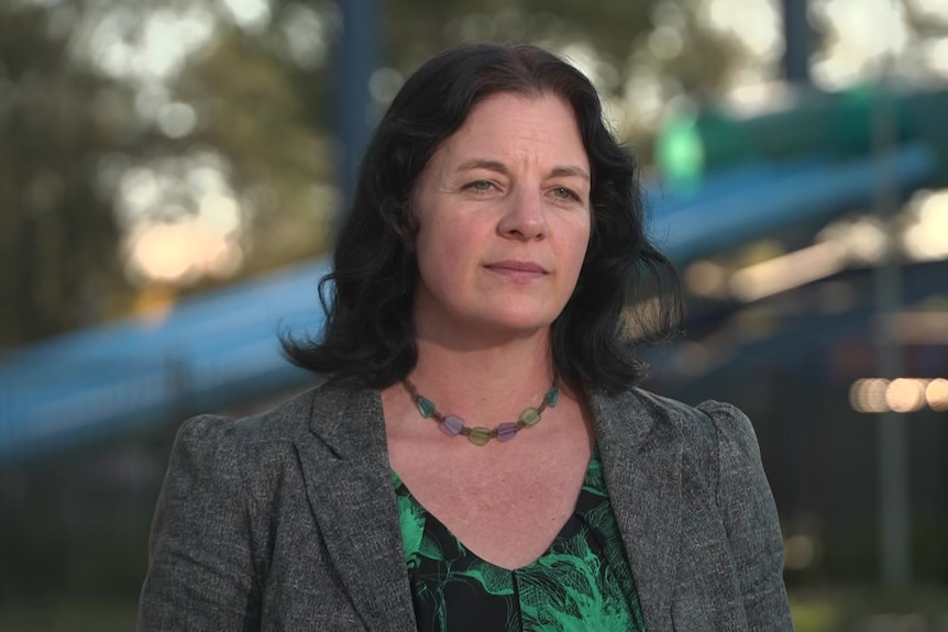 A woman with black hair stands outside a derelict water park.