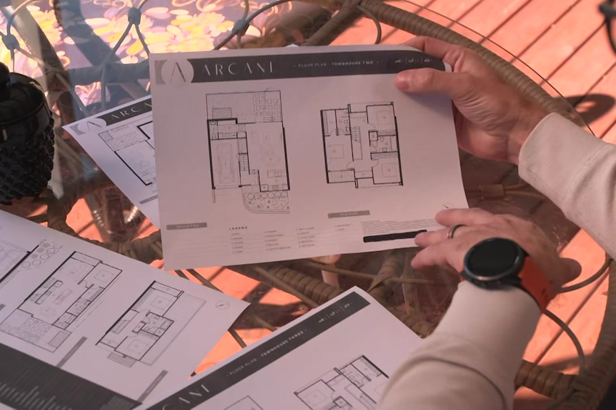 Design plans of an off-the plan project scattered on a table, with a man's hands flicking through them.