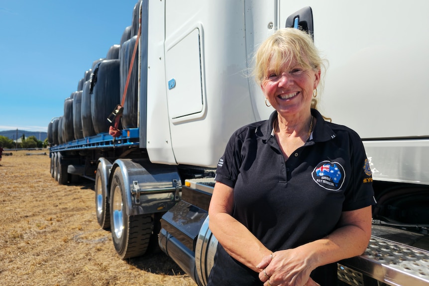 A blonde woman leaning against a white track that is carrying hay bales.