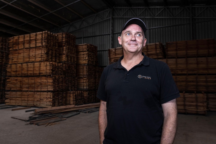 A man standing in a shed full of pallets of timber boards.