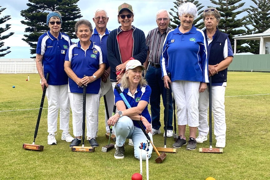 team photo of people grouped on lawn holding mallets with a hoop and balls on the grass