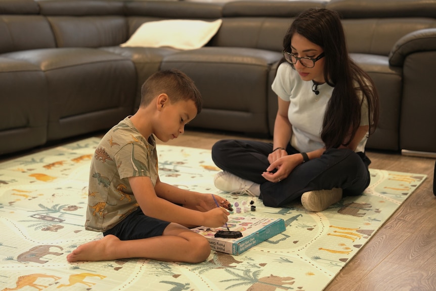 A young boy sitting on a loungeroom floor with a therapist, painting
