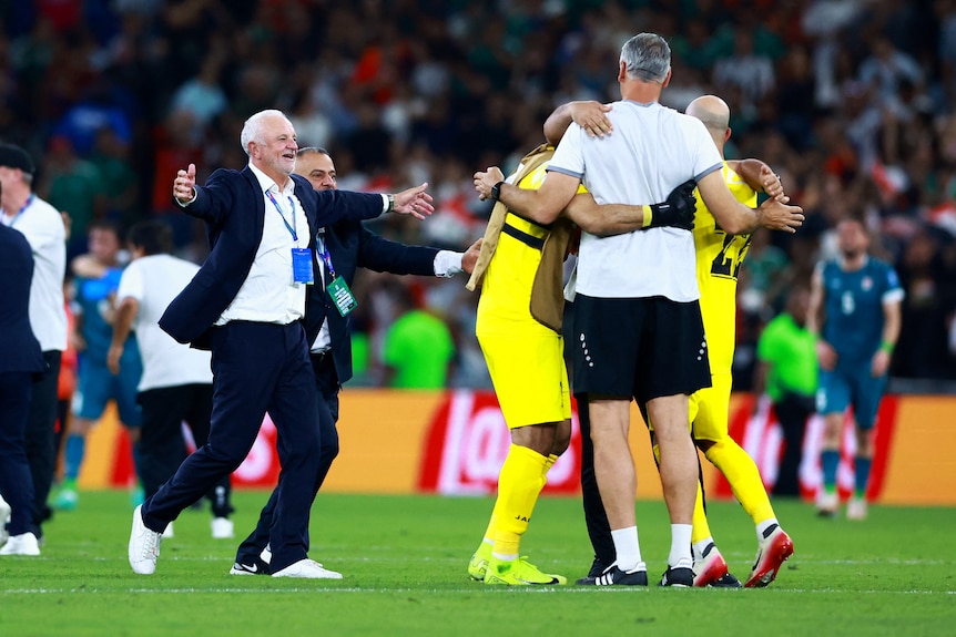 Players and coaches rush towards each other in celebration on a soccer field.