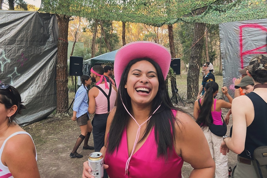 A woman wearing a pink outfit and cowgirl hat smiles to camera.
