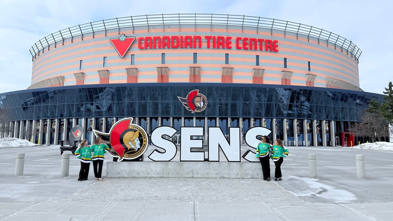 A group of girls stand around an Ottawa Sens logo outside an arena