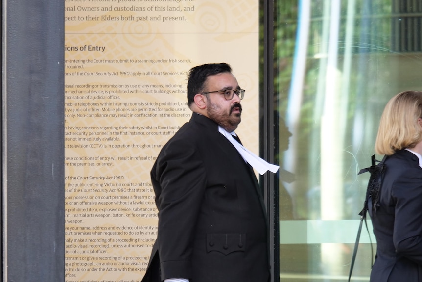 A dark-haired man in silks enters a court building.
