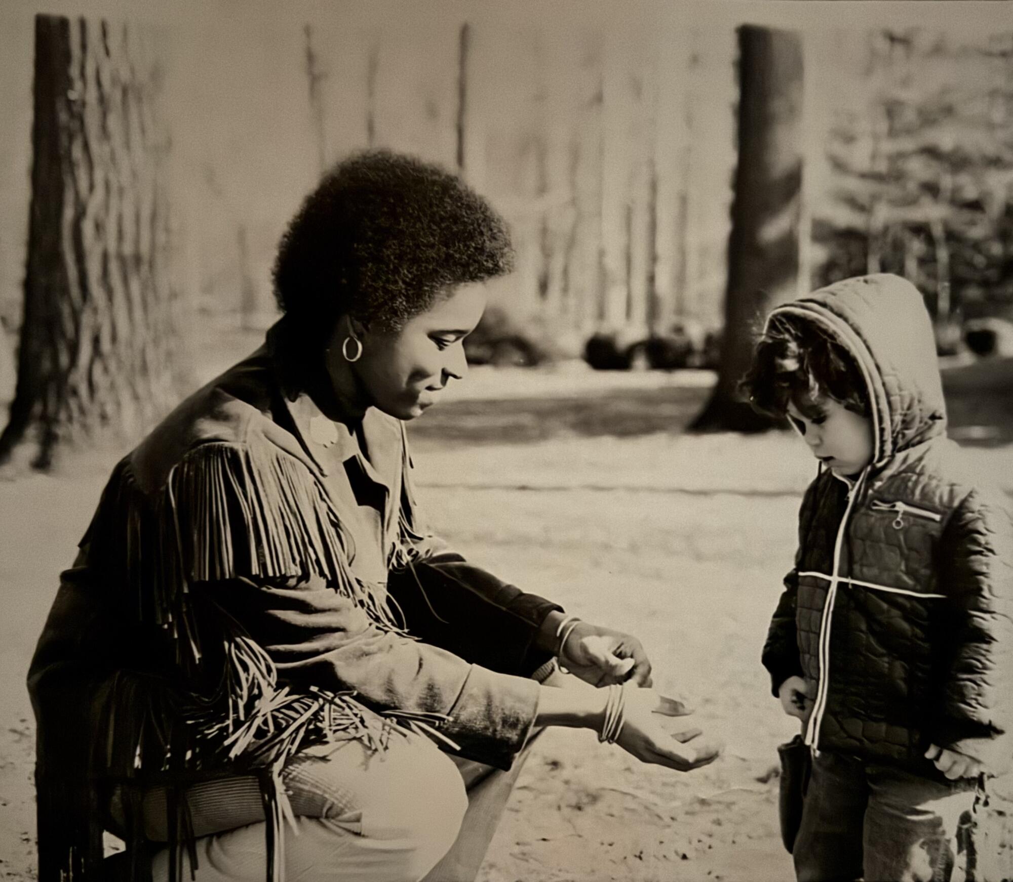 A smiling woman crouches and extends her hands to a child.
