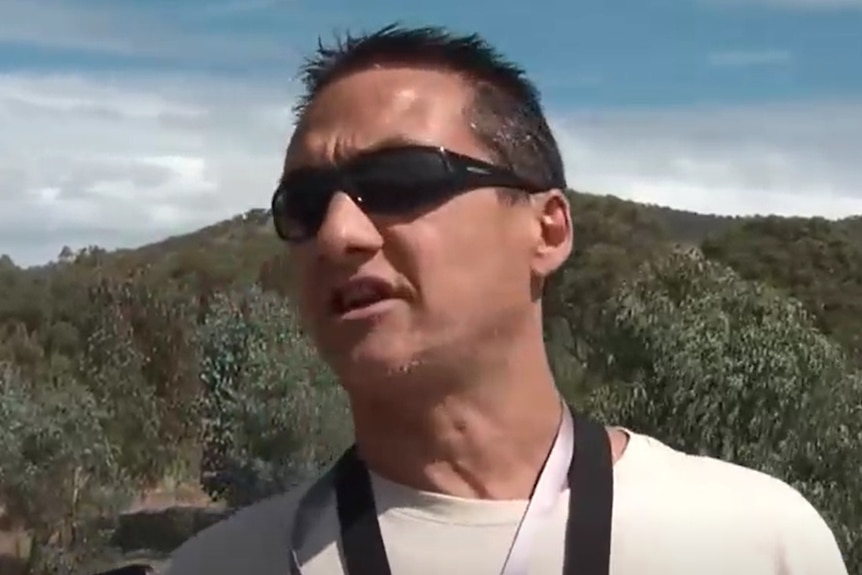 Screengrab from footage of Dezi Freeman wearing sunglasses and gesturing while speaking with police.