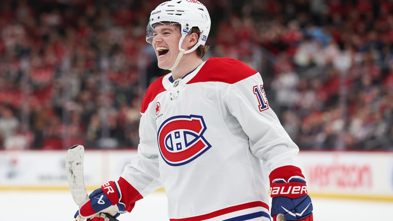 A male ice hockey player smiles during a game inside an arena filled with fans.