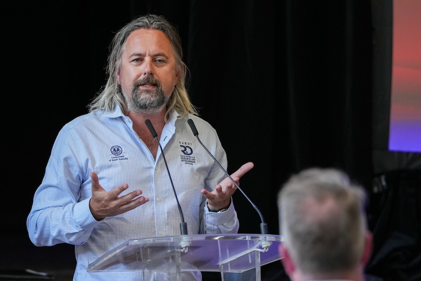 A man gestures his hands at a podium in front of people listening