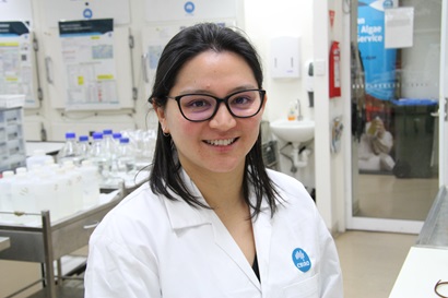 Researcher in lab coat wearing glasses and smiling at the camera.