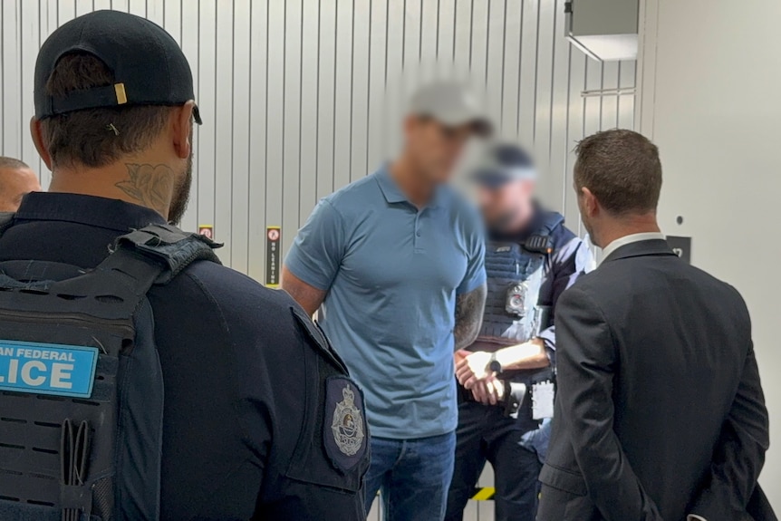 A man with a blurred face is arrested by uniformed police officers.