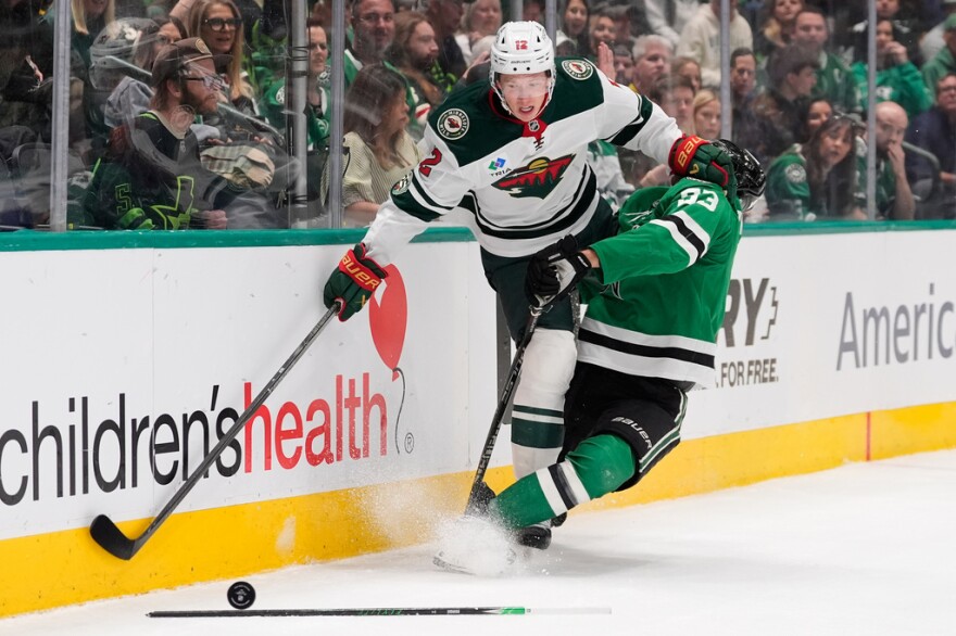 Two hockey players on opposing team collide against the boards.