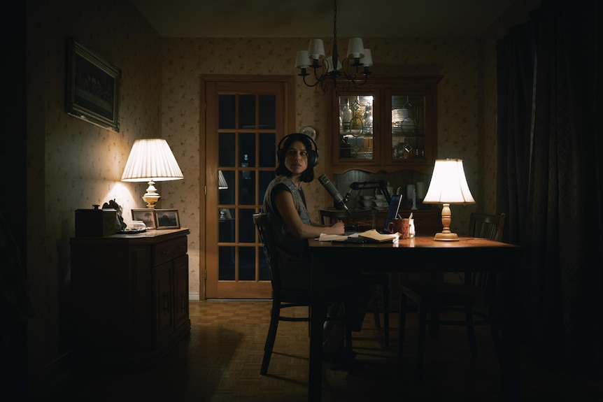 A woman sits in a study with recording equipment.