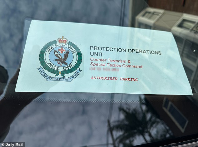 15740553 Meghan is flanked by police as she dons a blue baseball cap and sunnies for iconic coastal walk in Sydney ahead of $3,200-a-head Her Best Life retreat appearance