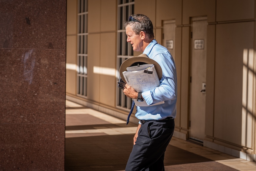 A man in a blue shirt and tie leaves court carrying his hat