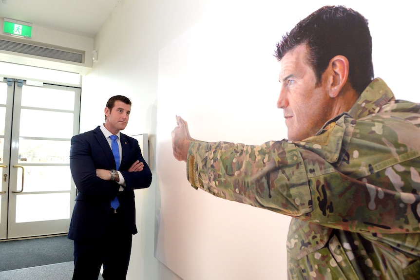 a man leaning against a wall which holds a portrait of him wearing an army uniform
