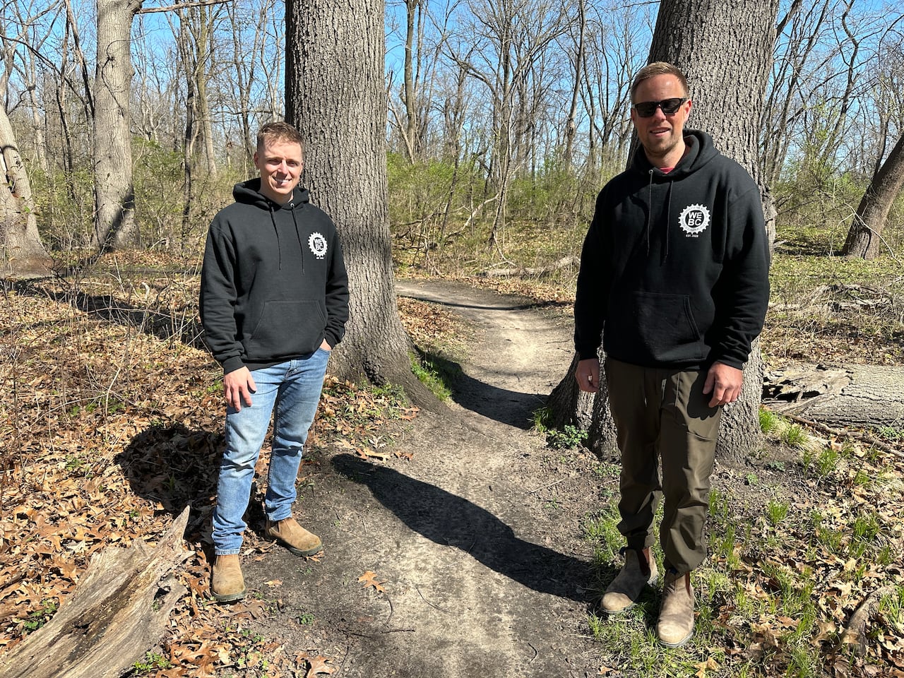 Two men in outdoor gear next to a bike trail.