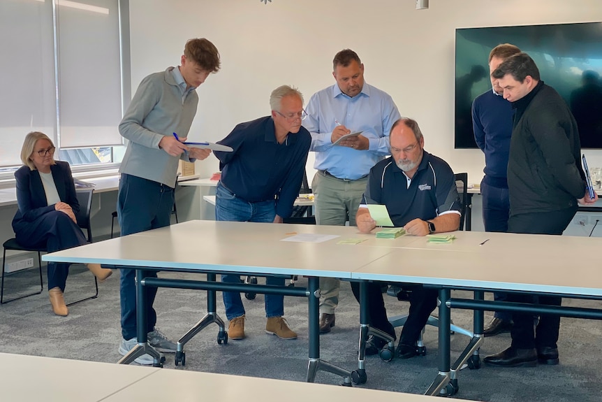 A man sitting down counts votes at a table while four other men look on