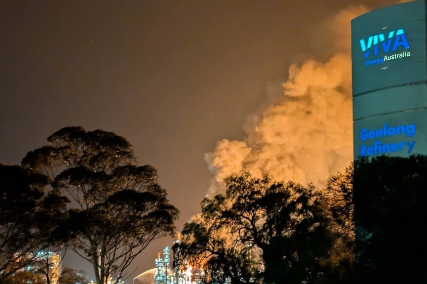 A phone photo of smoke lit up on the skyline behind a Viva Energy sign.