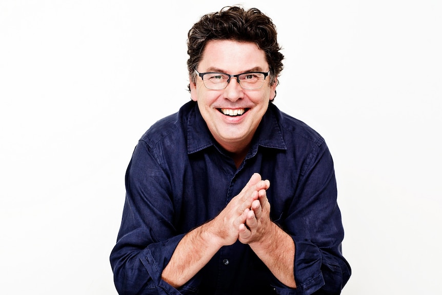 a man sitting down smiling while clasping his hands together