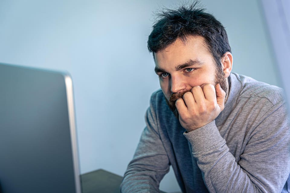 Tired bearded man looks at the computer screen.