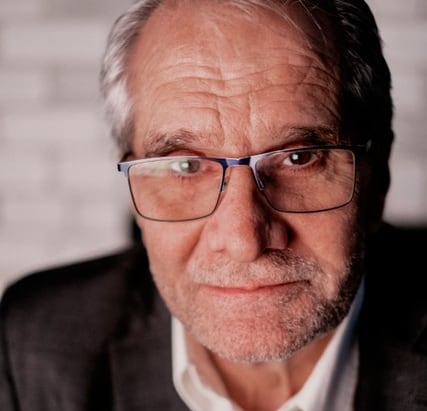 A man with glasses looks serious.