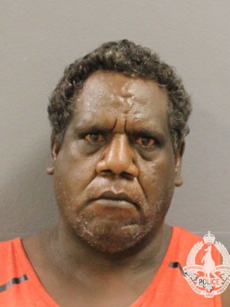 A mugshot of an Aboriginal man, serious expression looking directly at camera, yellow / orange pigment behind brown eyes.