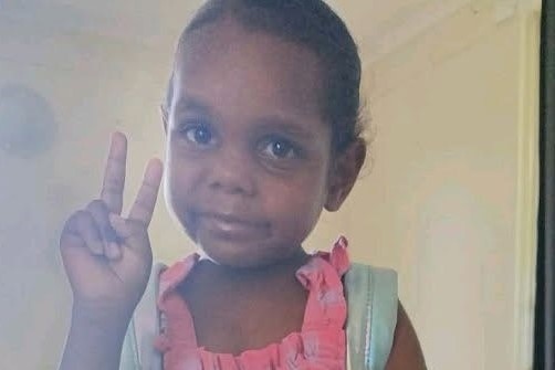 Young girl in pink dress does peace sign with fingers 