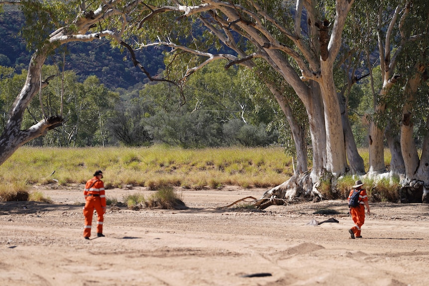 Two emergency service workers walk along dry creek bed in orange uniforms