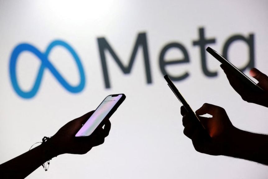 A silhouette of three hands holding mobile phones in front to Meta signage.