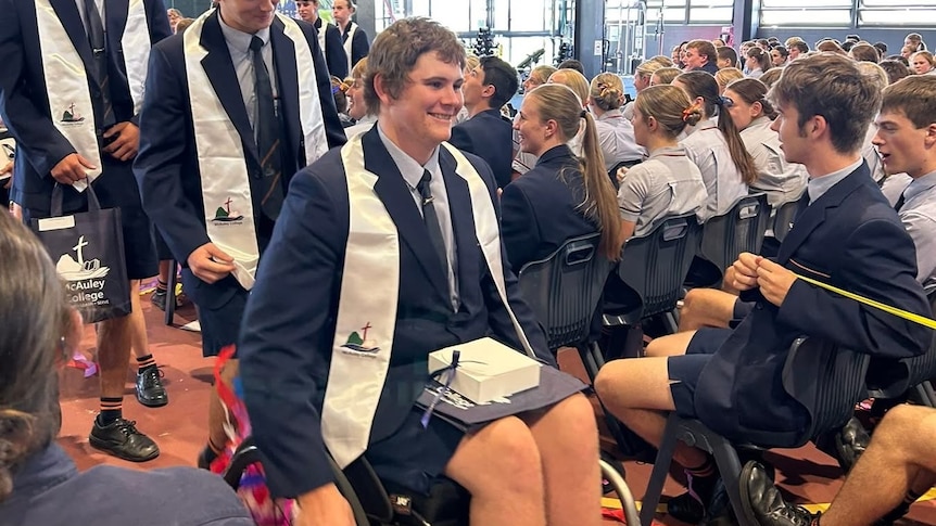 A man in a wheelchair graduating on stage at a school.