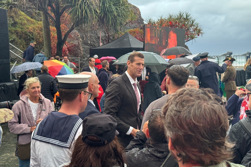 Ben Roberts-Smith shakes hands with supporters in a crowd on a rainy day. 