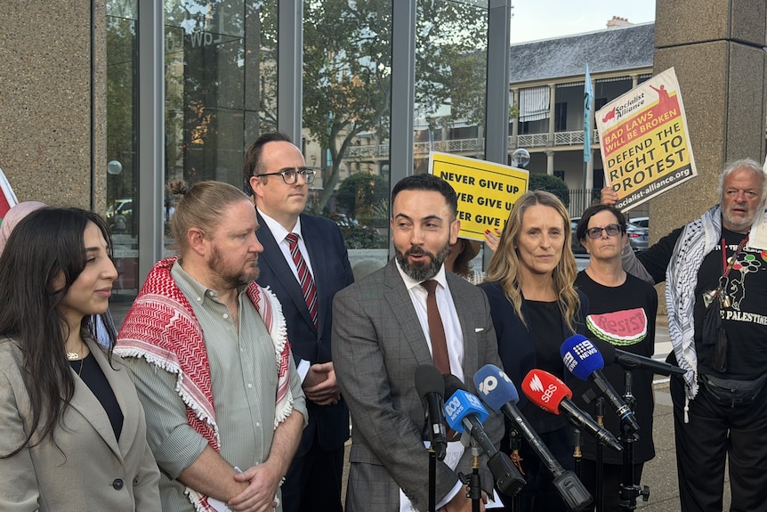 A group of people stand behind microphones outside court.