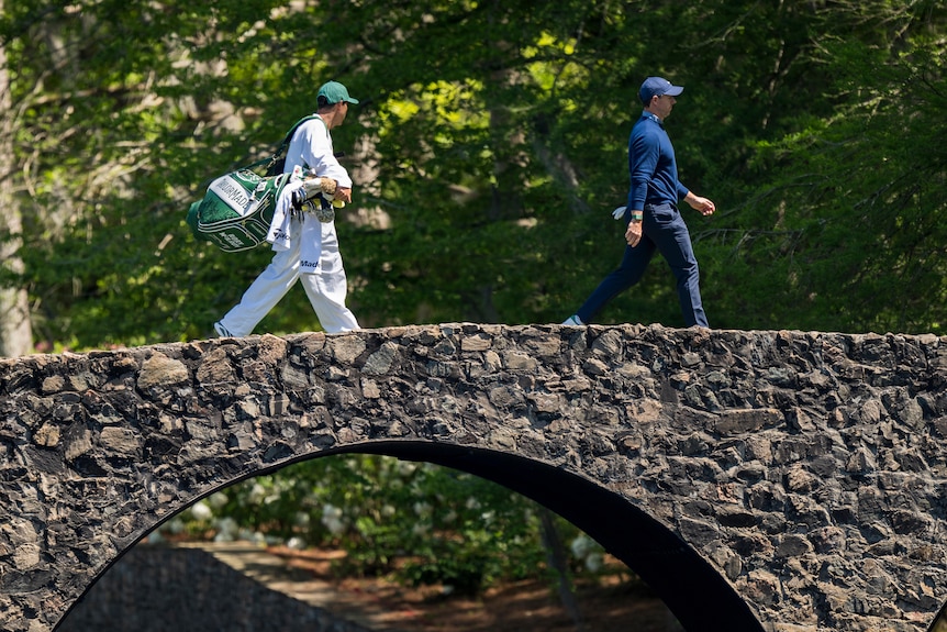Rory McIlroy walks across Hogan Bridge at the Masters with his caddy.