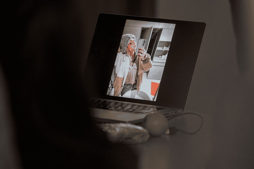 A photo of a woman wearing a beige jacket and grey hoodie on a laptop screen