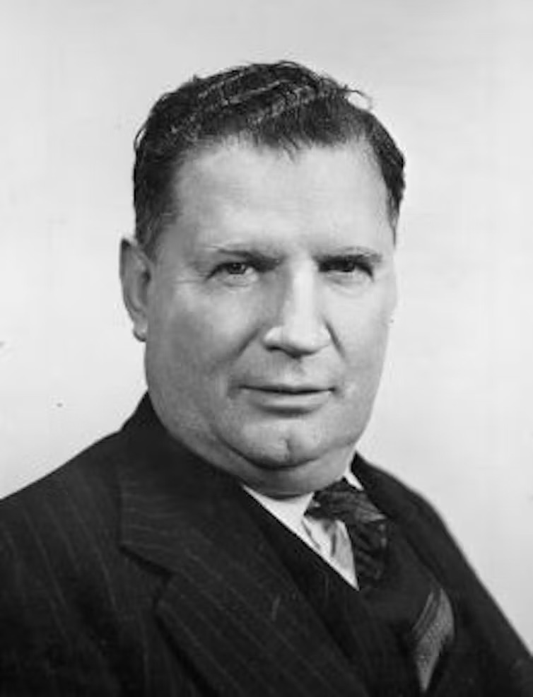 A black-and-white portrait of a heavy-set, slightly unkempt man with a wonky tie.