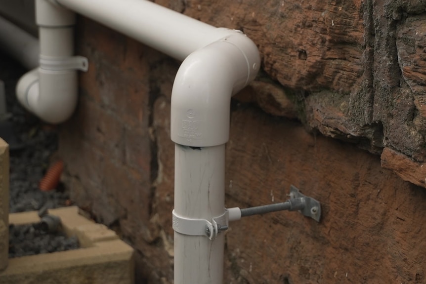 A pipe affixed to the outer wall of a brick building.