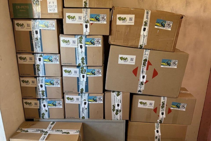Boxes stacked high against a wall filled with 3D printed parts