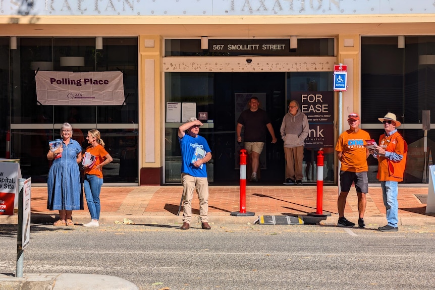 People in coloured shirts offer voting cards outside a voting venue.