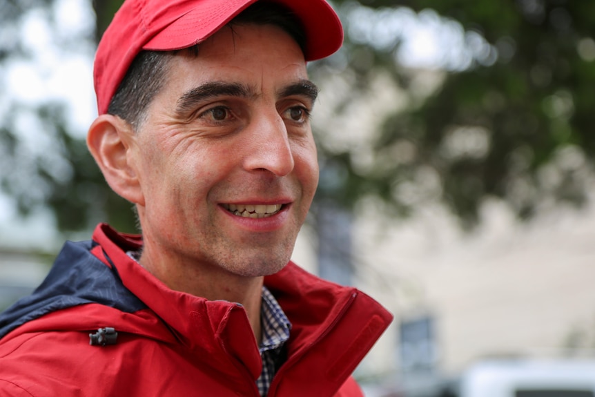 A man wearing red smiles at someone beyond the photo.