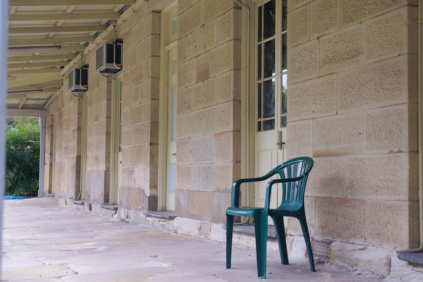 a green plastic chair sitting on the outdoor verandah of a sandstone building