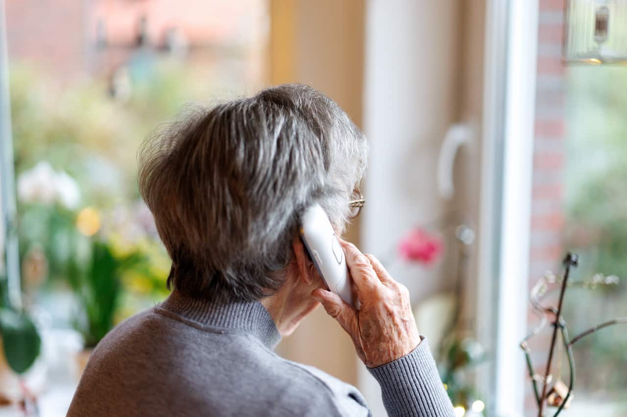 An older woman holds a phone to her ear