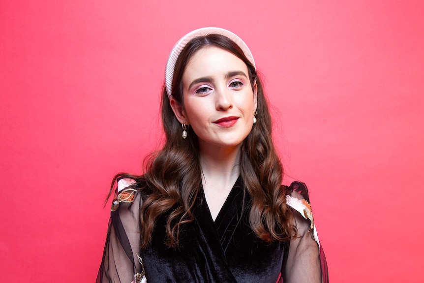 A woman is dressed in black standing against a pink background.