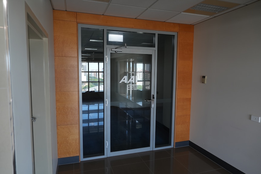 A wide shot of a hallway, showing an office door with the words AAI printed on it, looks empty, dark inside