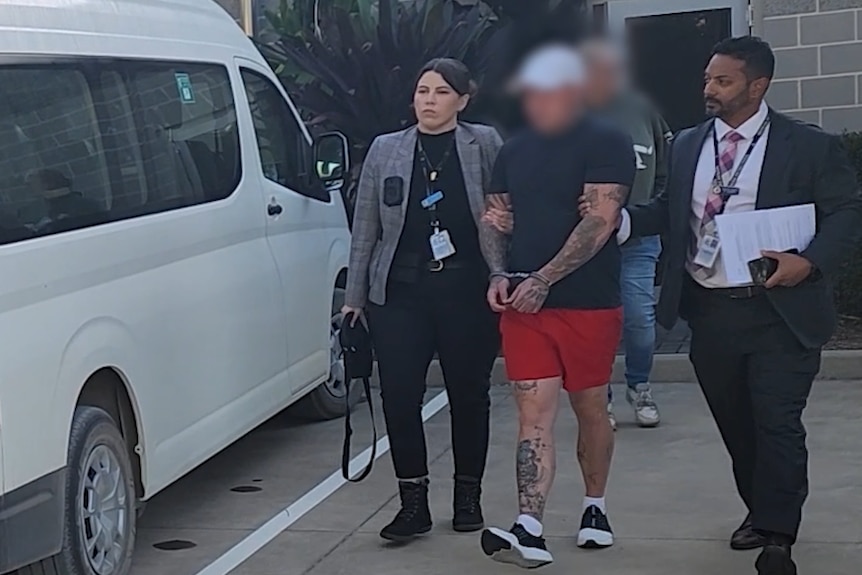 A man with a blurred face in handcuffs being escorted by police.